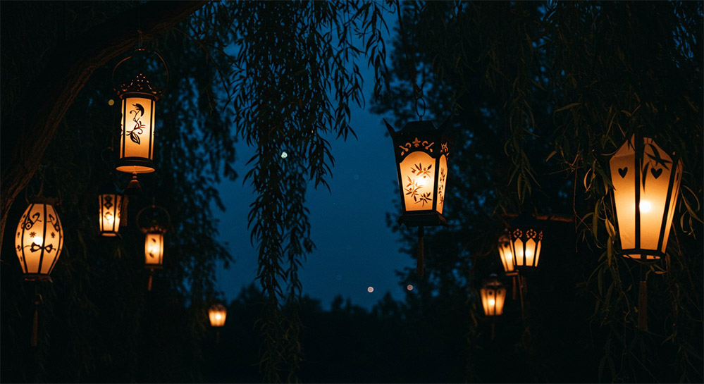 a few lanterns hanging from tree branches at different heights, little dark night